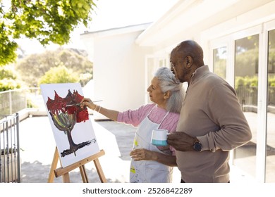 Diverse senior woman painting on canvas and senior man holding cup of coffee on sunny terrace. Lifestyle, retirement, senior lifestyle, nature, creativity, togetherness and domestic life, unaltered. - Powered by Shutterstock