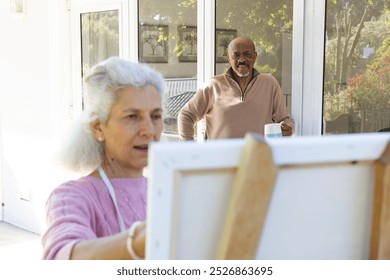 Diverse senior woman painting on canvas and senior man drinking coffee on sunny terrace. Lifestyle, retirement, senior lifestyle, nature, creativity, togetherness and domestic life, unaltered. - Powered by Shutterstock