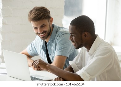 Diverse Smiling Businessmen Watching Funny Video Using Laptop Together, African And Caucasian Coworkers Having Fun Talking Looking At Computer Screen, Multiracial Office Workers Enjoy Online Teamwork