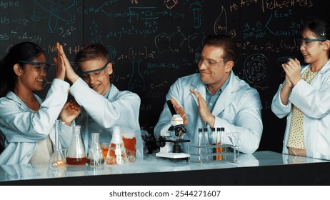 Diverse student clap hands while teacher show thumb to celebrate successful experiment. Edification.. Caucasian teacher looking after highschool children doing experiment at blackboard. Edification. - Powered by Shutterstock