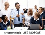 Diverse students and teacher in a science lab. Group of students learning chemistry. Teacher explaining experiment. Students wearing safety goggles. Teacher teaching a diverse high school class.