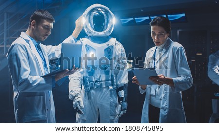 Diverse Team of Aerospace Scientists and Engineers Wearing White Coats have Discussion, Use Computers, Design New Space Suit Adapted for Galaxy Exploration and Travel. Constructing Astronaut Suit