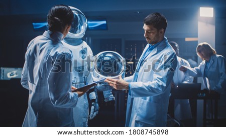 Diverse Team of Aerospace Scientists and Engineers Wearing White Coats have Discussion, Use Computers, Construct Astronaut Helmet for New Space Suit Adapted for Galaxy Exploration and Travel.