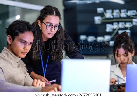 A diverse team of AI developers collaborates on a night coding session. A senior engineer oversees his team, intensely focused on debugging a complex machine learning project.