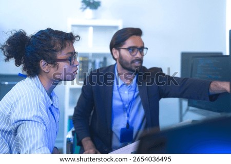 Diverse team of AI developers collaborating in a modern office. Indian male leading a discussion with Asian and Hispanic female colleagues on a machine learning project.