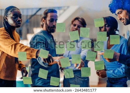 Diverse team analyzing project plan using sticky notes on glass wall during a productive meeting in modern office