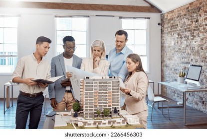 A diverse team of architects working on a building model together inside the office. A group of engineers planning a reconstruction or design project of an apartment block with blueprint documents - Powered by Shutterstock