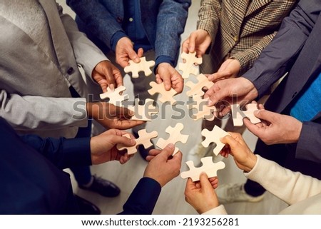 Diverse team of business people trying to solve problems all together. Group of multiracial men and women put different pieces of wooden jigsaw puzzle together. Teamwork concept. Conceptual