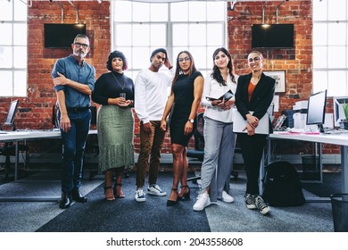 Diverse team of businesspeople standing together in an office. Group of modern businesspeople looking at the camera in a creative workplace. Business colleagues looking cheerful. - Shutterstock ID 2043558608