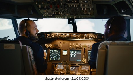 Diverse team of captain and copilot using dashboard command to takeoff and fly airplane. Pushing buttons to switch altitude and longitude on control panel in cockpit. Handheld shot.