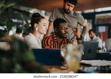 Diverse team collaborating in a coffee bar meeting, focused on working together on a laptop, sharing ideas and discussing projects - Powered by Shutterstock