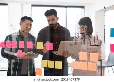 Diverse team collaborating on project using sticky notes and graphs. Conducting brainstorming session in modern office setting. Focused on achieving business success through teamwork and innovation. - Powered by Shutterstock