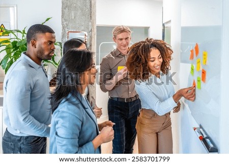 Diverse team collaborating, using sticky notes on a whiteboard during a brainstorming session in a modern coworking office