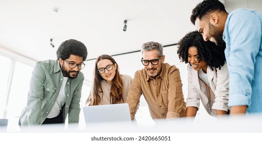 A diverse team of colleagues enthusiastically engages with content on a laptop, capturing a collaborative work culture and an effective brainstorming session in a contemporary office - Powered by Shutterstock