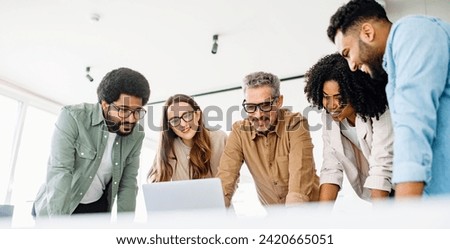 A diverse team of colleagues enthusiastically engages with content on a laptop, capturing a collaborative work culture and an effective brainstorming session in a contemporary office