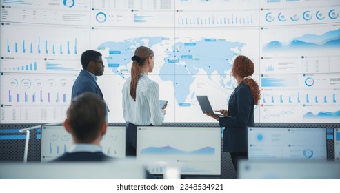 Diverse Team Of Data Science Department Discussing New Markets In Front of Big Digital Screen With World Map In Monitoring Office. Multiethnic Employees Working Behind Computers For Consulting Company - Powered by Shutterstock