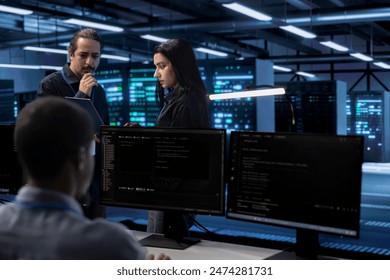 Diverse team of developers in data center using diagnostic tools and system monitoring software to identify root cause of errors. Multiracial employees in server farm mending equipment together
