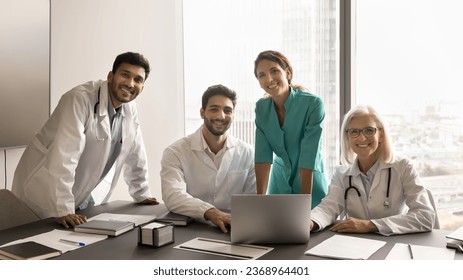 Diverse team of different aged doctors meeting at computer, looking at camera with toothy smile, posing for group professional portrait. Medical colleagues enjoying collaboration, teamwork - Powered by Shutterstock