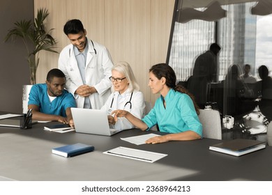 Diverse team of doctors meeting at laptop for medical discussion, using Internet job communication service, sitting at table with computer, talking, consulting mature chief, mentor - Powered by Shutterstock