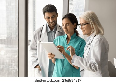 Diverse team of doctors meeting at tablet computer, using medical online service, communication, discussing application, patient test electronic results, using technology for effective teamwork - Powered by Shutterstock