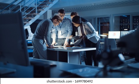Diverse Team of Electronics Development Engineers Standing at the Desk Working with Documents, Solving Project Problems Late at Night. Specialists Working on Ultra Modern Industrial Design.