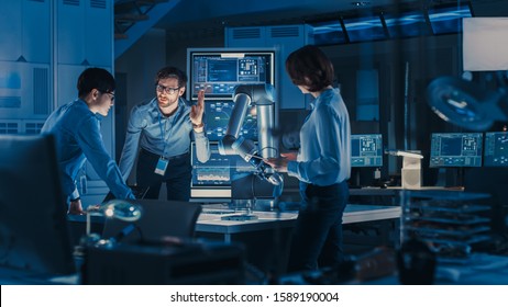 Diverse Team of Engineers with Laptop and a Tablet Analyse and Discuss How a Futuristic Robotic Arm Works and Moves a Metal Object. They are in a High Tech Research Laboratory with Modern Equipment. - Shutterstock ID 1589190004