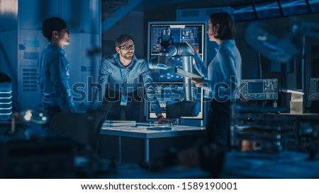 Diverse Team of Engineers with Laptop and a Tablet Analyse and Discuss How a Futuristic Robotic Arm Works and Moves a Metal Object. They are in a High Tech Research Laboratory with Modern Equipment.
