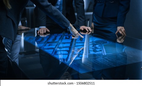 Diverse Team of Government Intelligence Agents Standing Around Digital Touch Screen Table and Satellite Tracking Suspect, Pointing at Display. Big Dark Surveillance Room. - Shutterstock ID 1506802511
