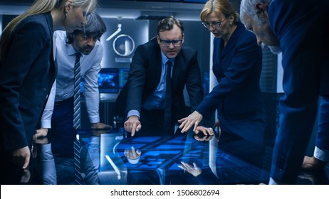 Diverse Team of Government Intelligence Agents Standing Around Digital Touch Screen Table and Tracking Suspect. FBI Agents Using Satellite Surveillance in the Dark Monitoring Room. - Shutterstock ID 1506802694