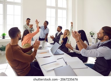 Diverse team of happy euphoric ecstatic mixed race multiethnic people sitting at office table, celebrating increasing sales, applauding their leader. Business, teamwork, success, recognition concept - Powered by Shutterstock