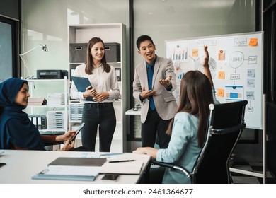 A diverse team, including a middle-aged Asian businessman, Caucasian young businesswoman, Muslim hijab-wearing middle-aged businesswoman, meets in a boardroom to close an Annual General Meeting. - Powered by Shutterstock