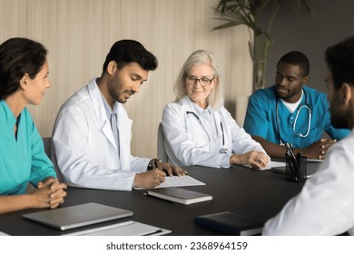 Diverse team of medical professionals making business decision on meeting with colleagues, partners. Confident young Indian chief doctor signing agreement, hiring new specialist - Powered by Shutterstock