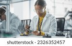 Diverse Team of Multiethnic Young Scientists Passing Internship in a Modern High Tech Laboratory. African Female Working with Soldering Iron Wearing Safety Goggles and White Lab Coat