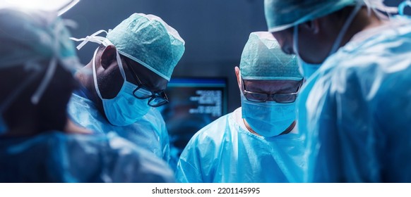 Diverse Team Of Professional Medical Surgeons Perform Surgery In The Operating Room Using High-tech Equipment. Doctors Work To Save A Patient In A Modern Hospital. Medicine, Technology And Healthcare.