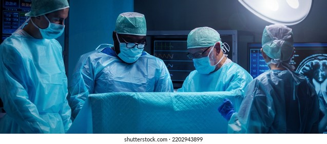 Diverse Team Of Professional Medical Surgeons Perform Surgery In The Operating Room Using High-tech Equipment. Doctors Work To Save A Patient In A Modern Hospital. Medicine, Technology And Healthcare.