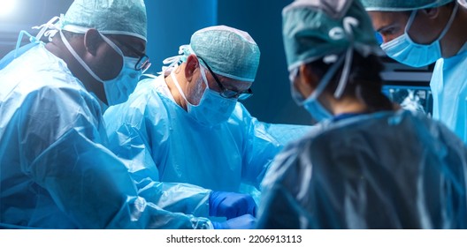 Diverse Team Of Professional Medical Surgeons Perform Surgery In The Operating Room Using High-tech Equipment. Doctors Work To Save A Patient In A Modern Hospital. Medicine, Technology And Healthcare.