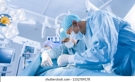 Diverse Team Of Professional Surgeon,  Assistants And Nurses Performing Invasive Surgery On A Patient In The Hospital Operating Room. Surgeons Talk And Use Instruments.