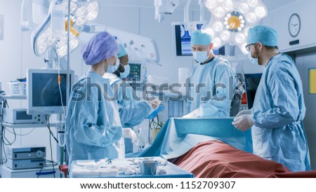 Diverse Team of Professional surgeon, Assistants and Nurses Performing Invasive Surgery on a Patient in the Hospital Operating Room. Surgeons Talk and Use Instruments. Real Modern Hospital