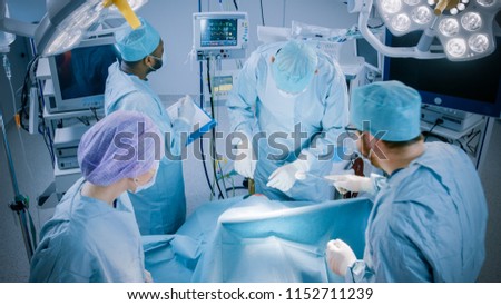 Diverse Team of Professional surgeon,  Assistants and Nurses Performing Invasive Surgery on a Patient in the Hospital Operating Room. Surgeons Talk and Use Instruments. Real Modern Hospital.