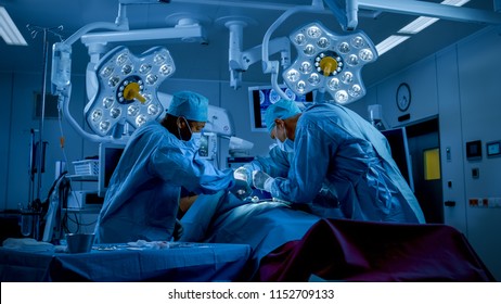 Diverse Team Of Professional Surgeons Performing Invasive Surgery On A Patient In The Hospital Operating Room. Surgeons Use Instruments. Dark And Cold Atmosphere.