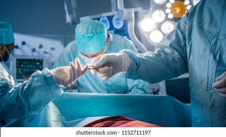 Diverse Team of Professional Surgeons Performing Invasive Surgery on a Patient in the Hospital Operating Room. Nurse Hands Out Instruments to surgeon, Anesthesiologist Monitors Vitals. Modern Hospital