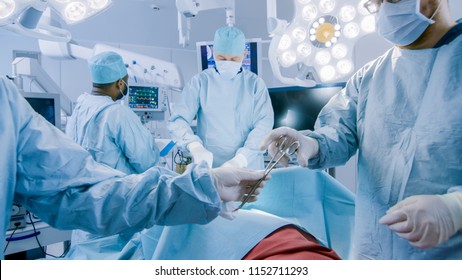 Diverse Team of Professional Surgeons Performing Invasive Surgery on a Patient in the Hospital Operating Room. Nurse Passes Instrument to a Chief Surgeon, Anesthesiologist Monitors Vitals.
