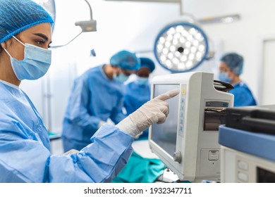 Diverse Team Of Professional Surgeons Performing Invasive Surgery On A Patient In The Hospital Operating Room. Nurse Hands Out Instruments To Surgeon, Anesthesiologist Monitors Vitals.