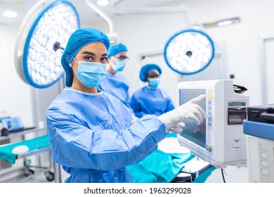 Diverse Team Of Professional Surgeons Performing Invasive Surgery On A Patient In The Hospital Operating Room. Nurse Hands Out Instruments To Surgeon, Anesthesiologist Monitors Vitals.