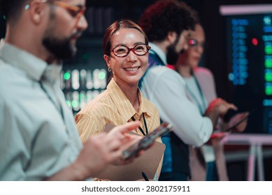 Diverse team of it professionals collaborating in a server room. Woman smiling at camera while colleague operates tablet