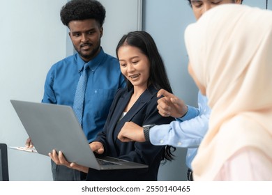 Diverse team of professionals working together, discussing ideas and reviewing information on a laptop during an office meeting. - Powered by Shutterstock