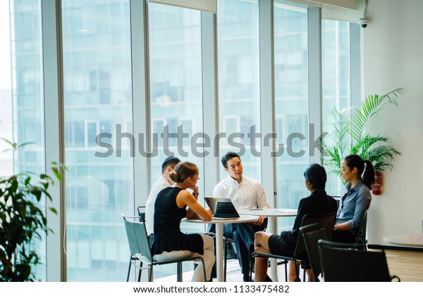 A diverse team sit around a table in a meeting\
room to have a business meeting to discuss plans. The group is\
international with Asian and White team members and they are all\
professionally dressed.