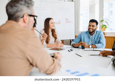 A diverse team sits at a table, engaging in a lively discussion with expressions of agreement and interest, epitomizing a productive brainstorming session in a bright, modern office setting - Powered by Shutterstock