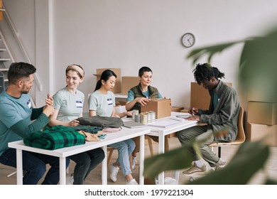 Diverse team of smiling volunteers organizing food and clothes during help and donations event, copy space - Powered by Shutterstock