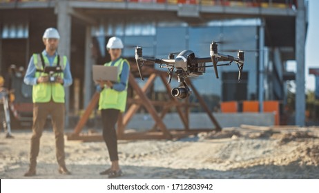 Diverse Team of Specialists Pilot Drone on Construction Site. Architectural Engineer and Safety Engineering Inspector Fly Drone on Commercial Building Construction Site Controlling Design and Quality - Powered by Shutterstock